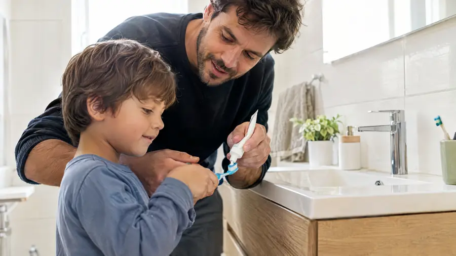 Padre ayudando a su hijo a poner pasta en el cepillo