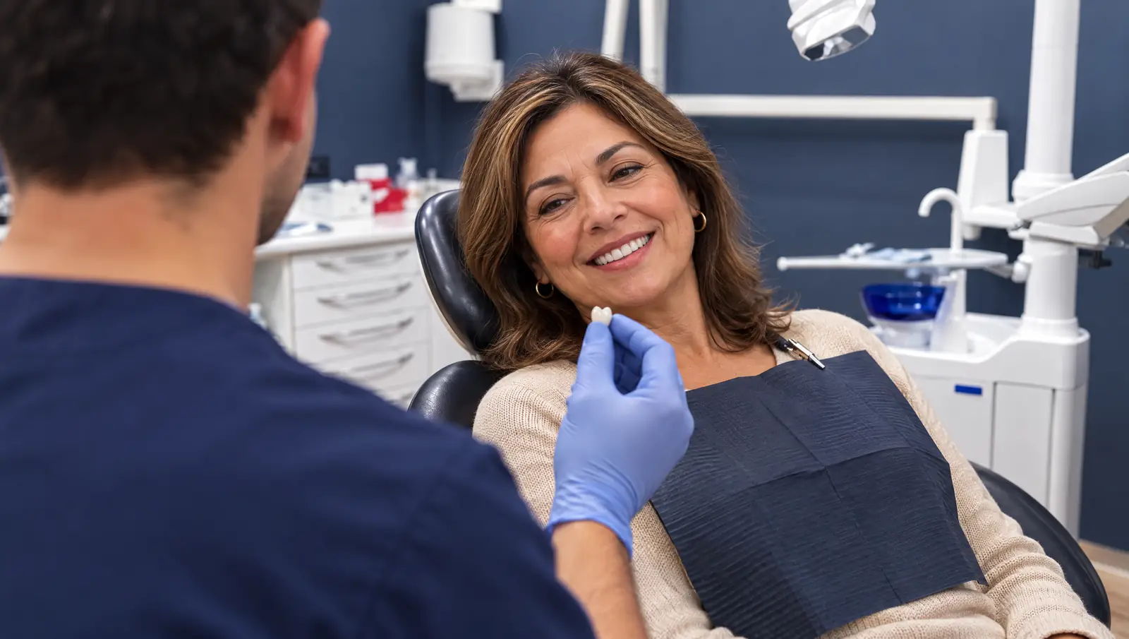 Paciente sonriendo mientras el odontólogo le enseña una corona de cerámica en Odontis Rivas