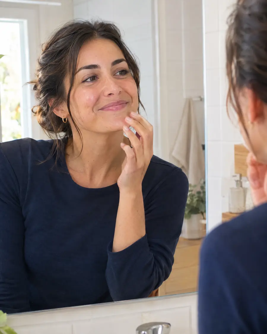 Mujer cohibida por su sonrisa gingival ante el espejo