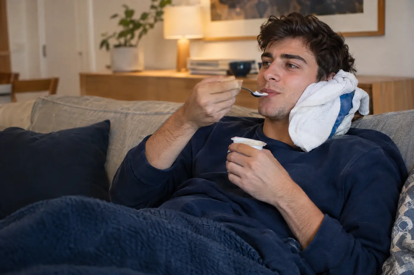 Chico recuperándose en el sofá con frío en la mandíbula y un yogur